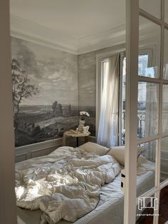 an unmade bed sitting in front of a window next to a painting on the wall