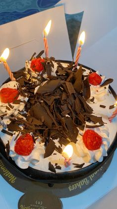 a birthday cake with white frosting and chocolate shavings topped with lit candles