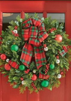 a christmas wreath on a red door with green and red ornaments hanging from the front