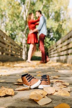 a man and woman standing next to each other on a wooden walkway with leaves all over the ground