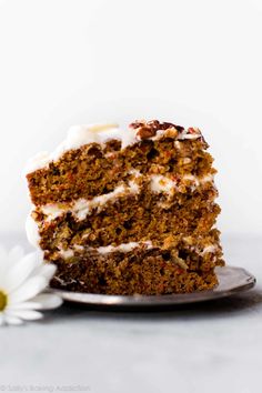 a slice of carrot cake with white frosting on a plate next to a flower