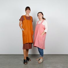 two women standing next to each other in front of a white wall wearing aprons