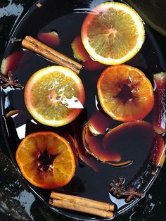 sliced oranges and cinnamon sticks are in a bowl with water on the table top