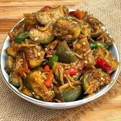 a white bowl filled with cooked vegetables on top of a wooden table next to a brown cloth