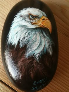 an eagle painted on a rock sitting on a wooden table next to a pen and pencil