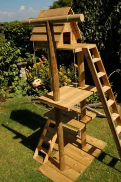 a wooden swing set in the grass with a ladder to it and a birdhouse on top