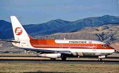 an orange and white jet airliner on runway with mountains in background