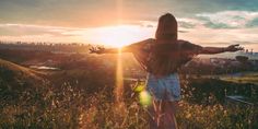 a woman standing on top of a lush green field next to the sun in the sky