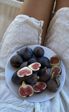 a white plate topped with sliced figs on top of a person's legs