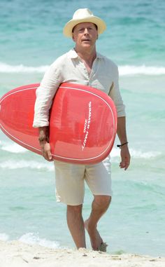 a man holding a red surfboard on top of a beach next to the ocean