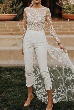 a woman standing in the grass wearing white pants and a sheer top with flowers on it