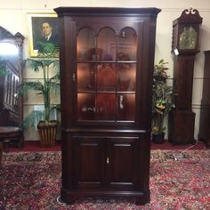 a tall wooden china cabinet sitting on top of a carpeted floor next to a clock