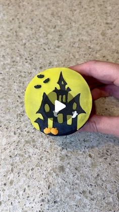 a hand holding a yellow and black painted rock with bats on it's face