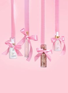 three bottles with pink ribbons hanging from them on a pink background in the shape of candles