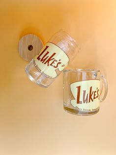 two coffee mugs are hanging on the wall, one is upside down and the other has a sticker that says mike's 1 likes