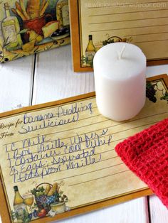 a white candle sitting on top of a wooden table next to two notepads