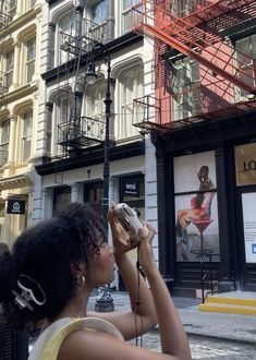 a woman standing in front of a fire escape on the side of a building while looking at her cell phone