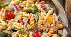 a plate of pasta salad with broccoli, tomatoes and other veggies