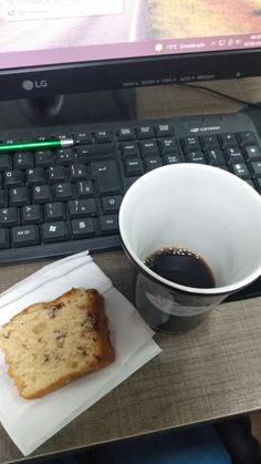 a cup of coffee next to a piece of cake and a laptop on a desk