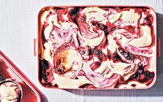 an ice cream sundae with cherries and blueberries in a red container on a white tablecloth