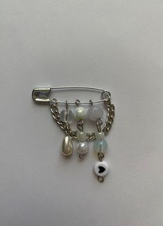 a hair clip with charms attached to it on a white surface, including pearls and beads