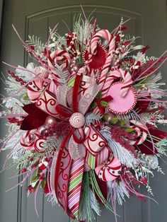 a christmas wreath with candy canes and other holiday decorations hanging on a front door