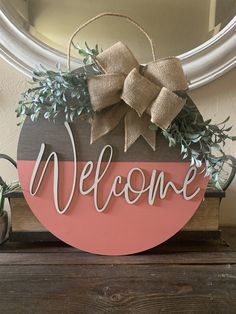 a welcome sign hanging from the side of a wooden door with a bow on it