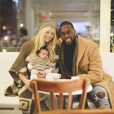 a man and woman sitting on a couch with a baby in their lap, smiling at the camera