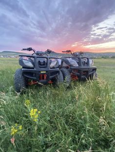 two atvs parked in the middle of a field with flowers and grass at sunset