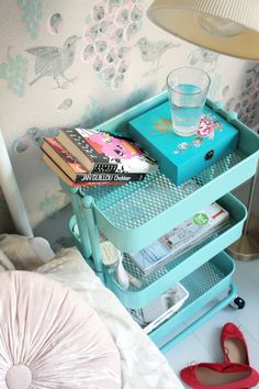 a blue tray with books and magazines sitting on top of a bed next to a lamp