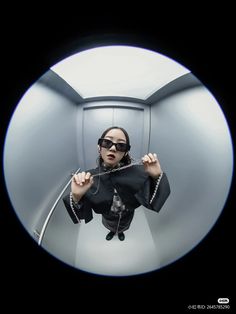 a woman in black jacket and sunglasses holding up her hands while looking through a mirror