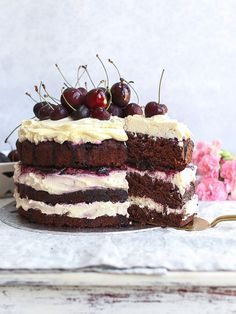 a cake with white frosting and cherries sitting on a table next to flowers