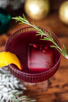 a close up of a drink in a glass on a table with pine cones and decorations