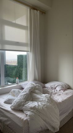 an unmade bed sitting in front of a window with white sheets and blankets on it