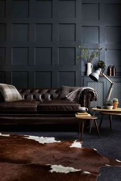 a brown leather couch sitting in a living room next to a wooden table and cowhide rug