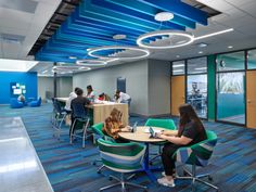 people sitting at tables in an office setting with blue and green accents on the ceiling