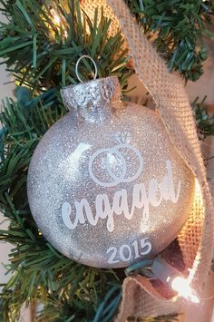 a silver ornament hanging from a christmas tree with the word engaged on it