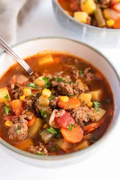 two bowls filled with meat and vegetable soup on top of a white tablecloth next to silverware