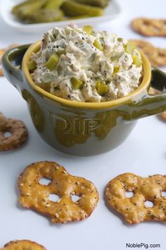 a bowl of dip surrounded by pretzels and crackers on a white table