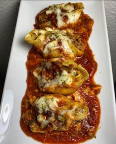 three stuffed shells covered in sauce on a white plate