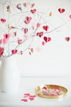 a white vase filled with pink hearts next to a plate and tree branch on a table