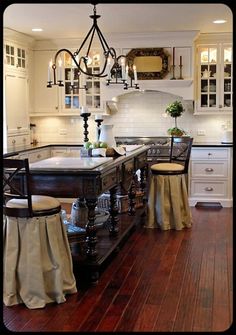 a large kitchen with white cabinets and wooden floors, an island in the center is flanked by two stools