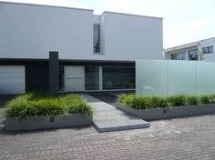 two large planters on the sidewalk in front of a modern house with white walls and windows