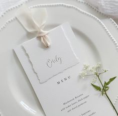 a white plate topped with a piece of paper next to a flower