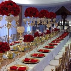 a long table with red flowers and gold place settings