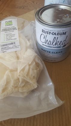 a can of paint next to a white cloth on top of a wooden table with a plastic bag