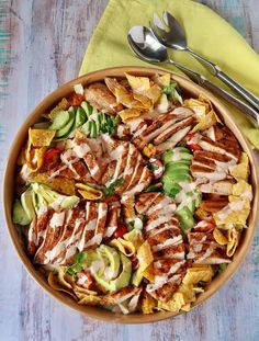 a bowl filled with chicken, lettuce and tortilla chips next to a fork