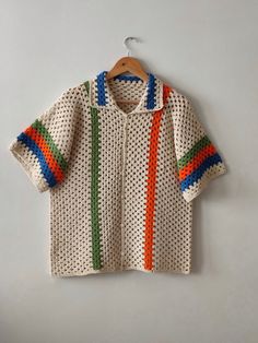 a knitted sweater hanging on a hanger next to a white wall with a green, red, orange and blue stripe