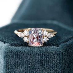 a pink diamond ring sitting on top of a blue velvet cushioned box with diamonds around it