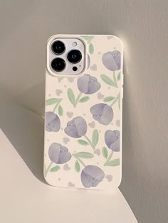 an iphone case sitting on top of a white table next to a wall with flowers painted on it